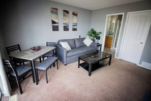 Ein Wohnzimmer mit grauem Sofa, einem Couchtisch, einem Esstisch mit Stühlen und einer Zimmerpflanze.