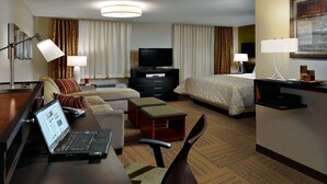 A hotel room with a bed, a desk with a laptop, a television, and a seating area with a chair and ottoman. - Accessible 1BR Suite w/ Kitchen | Pool + Breakfast (Johnson City)