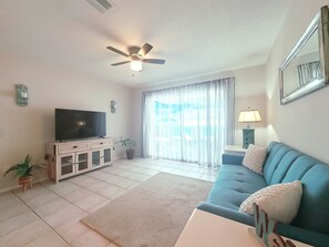 A living room with a flat-screen TV, a ceiling fan, a sofa, a coffee table, and a large window with curtains. - Conveniently located between Siesta key beach and downtown Sarasota.2/1 unit. (Sarasota)