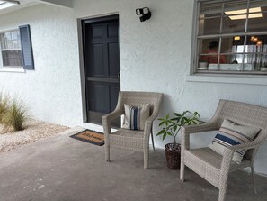 A house exterior with a black door, two wicker chairs with cushions, a potted plant, and a concrete porch. - Conveniently located between Siesta key beach and downtown Sarasota.2/1 unit. (Sarasota)