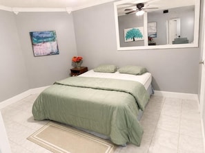 Ein Schlafzimmer mit einem Bett, einem Nachttisch, einem Spiegel und Kunstwerken an der Wand.