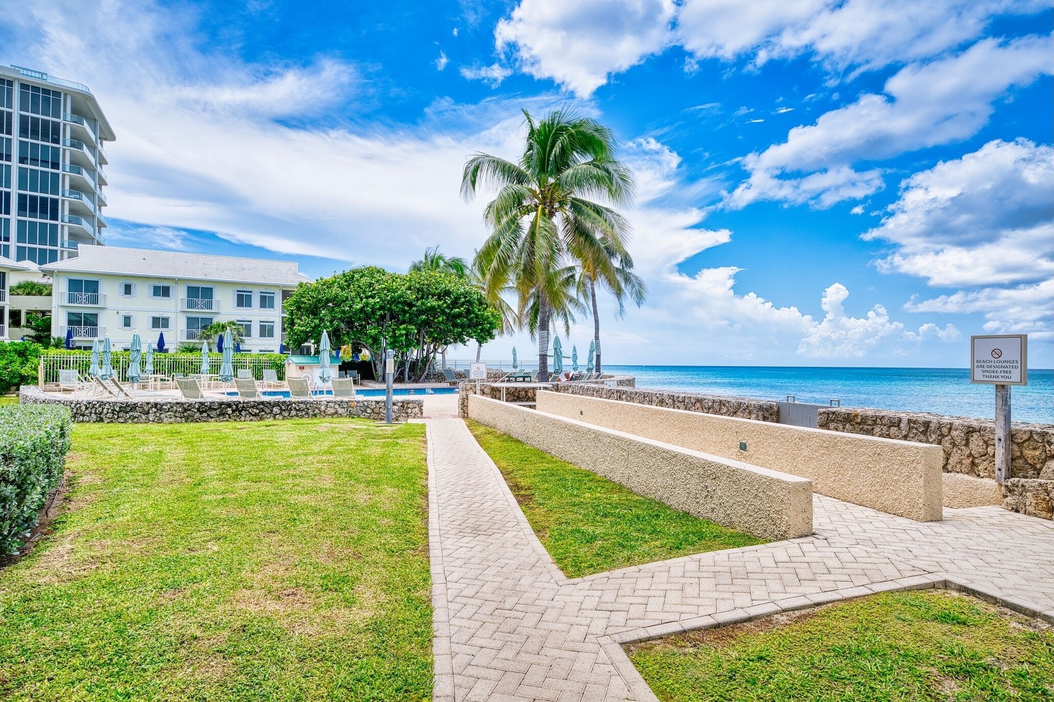 Un hotel frente a la playa con piscina, palmeras y cielo despejado.