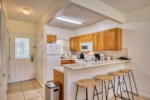 Une cuisine compacte avec des meubles en bois, un plan de travail blanc, un four à micro-ondes, une cuisinière et des tabourets de bar.
