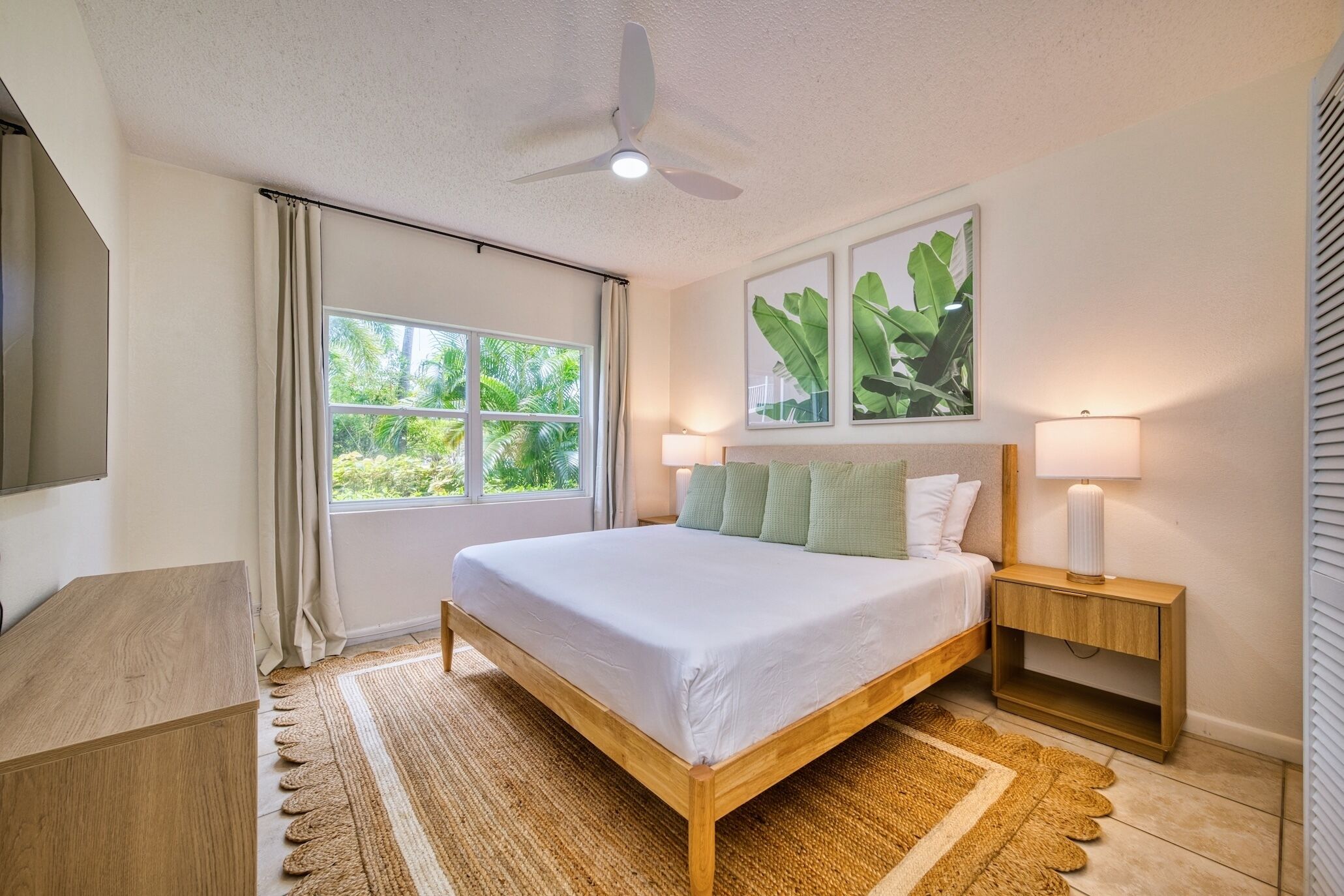Une chambre à coucher avec un lit, des tables de chevet, un ventilateur de plafond et une fenêtre avec des rideaux.