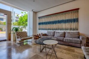 Een moderne woonkamer met een bank, fauteuil en salontafel, een groot abstract schilderij aan de muur, en uitzicht op het groen door een groot raam.