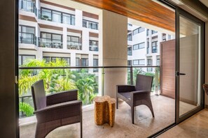 A balcony with wicker chairs and a small round table, overlooking a residential area with multiple buildings. - Ipana 1BR | Rooftop Pool & Parking | Near 5th Ave (Playa del Carmen)