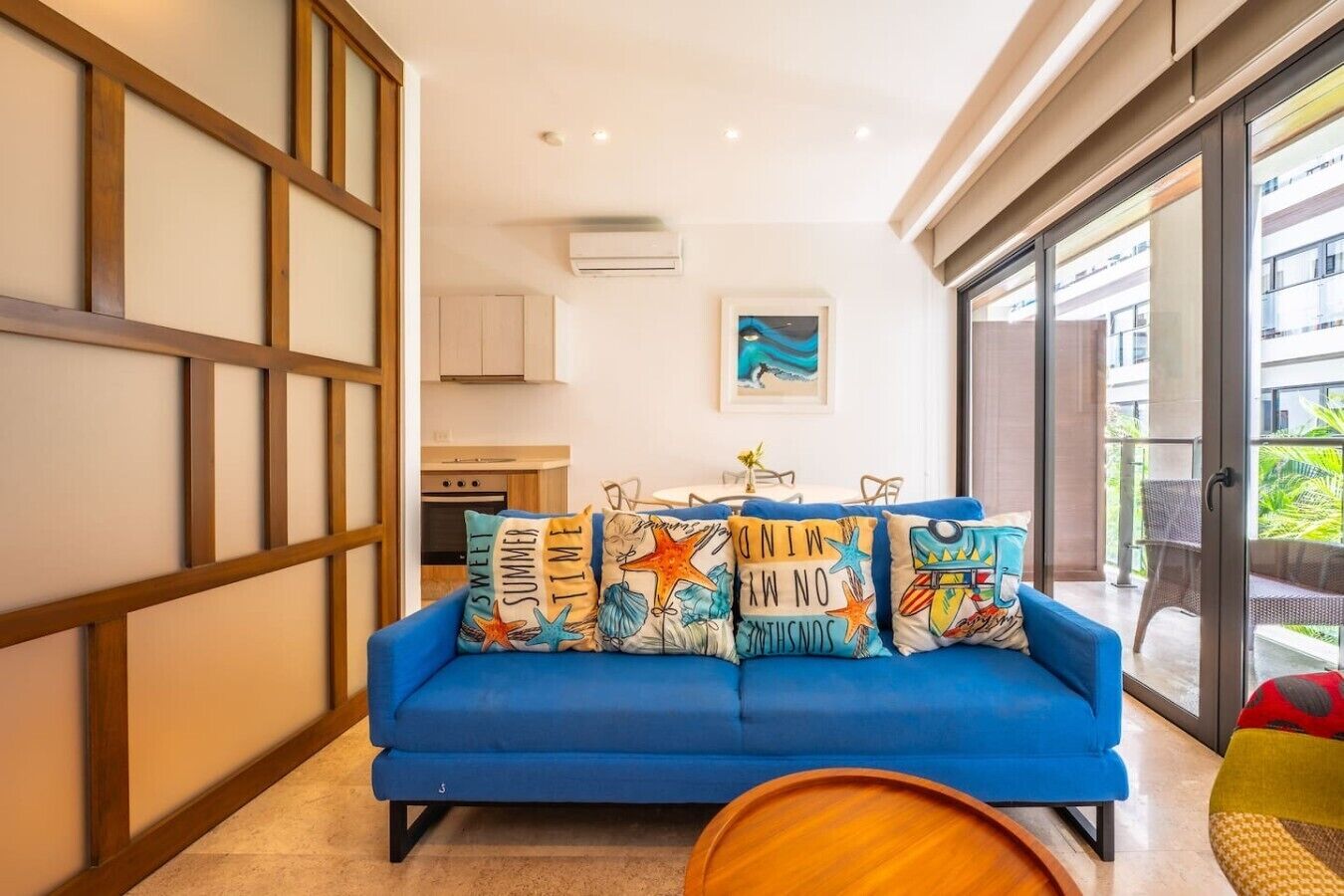 Ein blaues Sofa mit bunten Kissen in einem Raum mit einer Schiebetür, die auf einen Balkon führt.