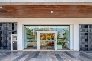 A modern building entrance with a glass facade, a wooden ceiling, and a metal gate on the left. - Ipana 1BR | Rooftop Pool & Parking | Near 5th Ave (Playa del Carmen)