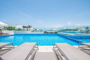 A rooftop swimming pool with clear blue water, surrounded by lounge chairs and a glass railing. - Ipana 1BR | Rooftop Pool & Parking | Near 5th Ave (Playa del Carmen)