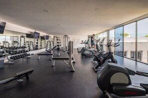 Een sportschool met diverse fitnessapparaten, grote ramen en een persoon die op een loopband aan het trainen is.