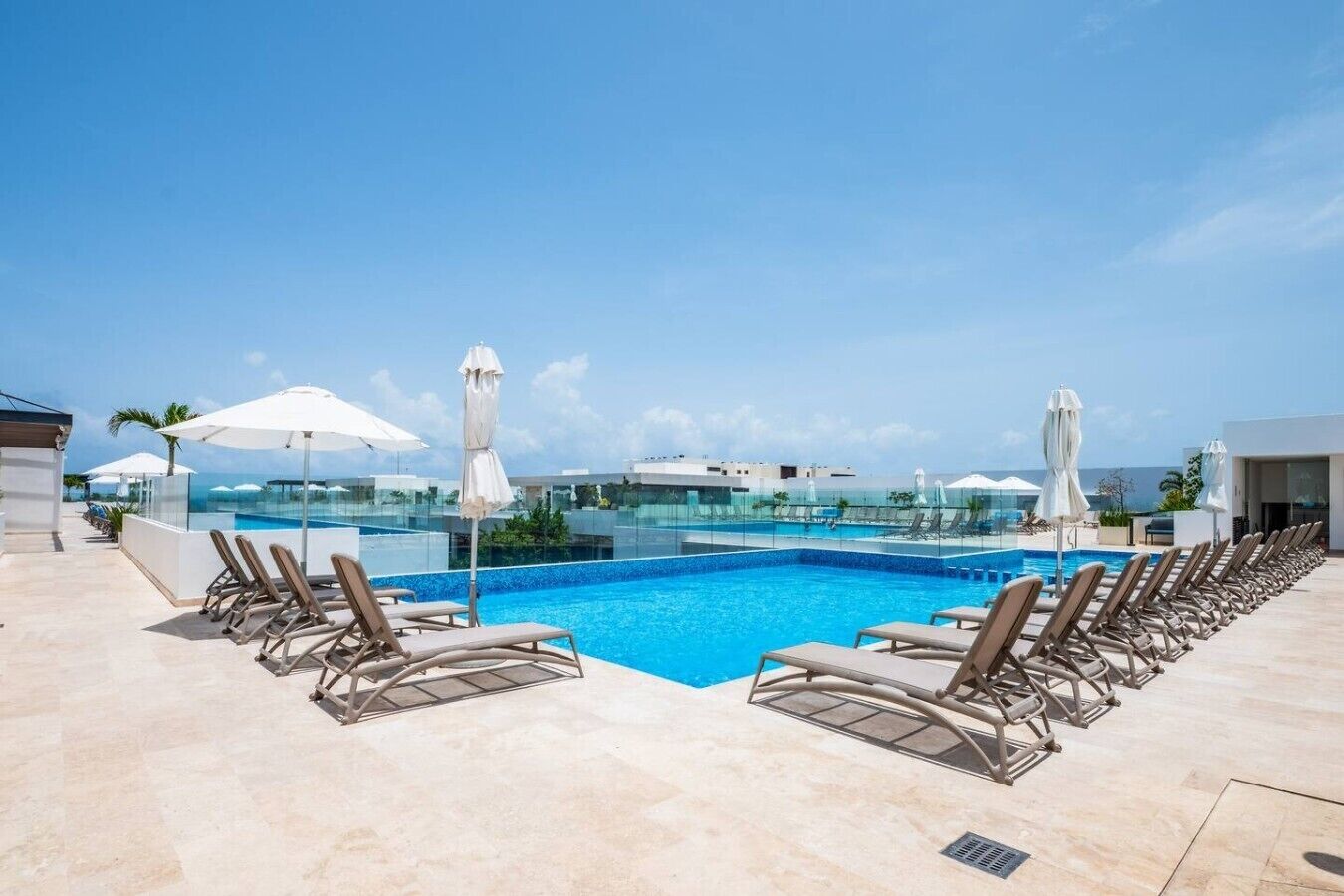 Un espace piscine aménagé sur le toit, avec des chaises longues et des parasols, offrant une vue sur un ciel bleu dégagé.