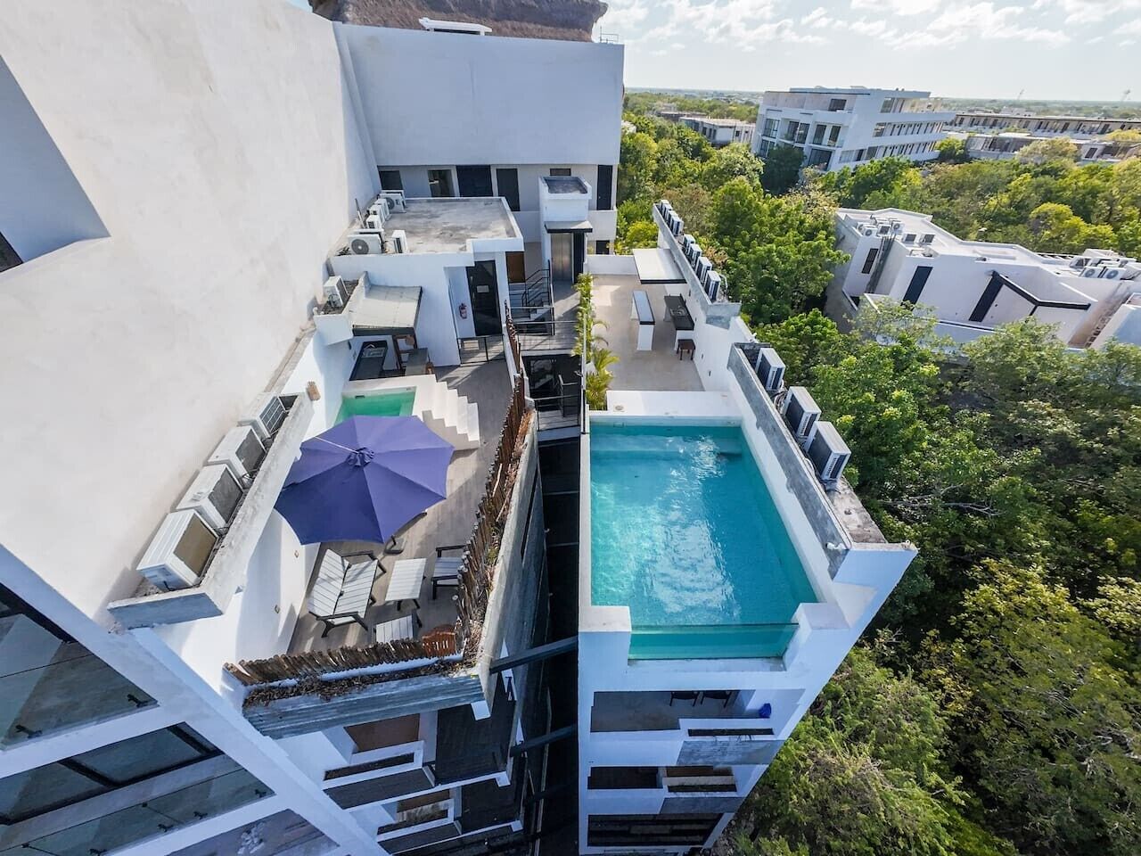 A rooftop pool area with a blue pool, sun loungers, and a purple umbrella.