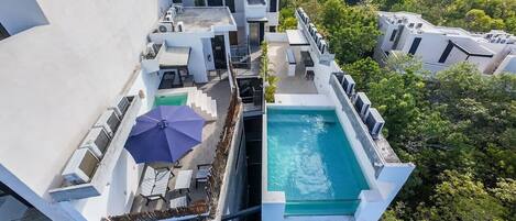 A rooftop pool area with a blue pool, sun loungers, and a purple umbrella.