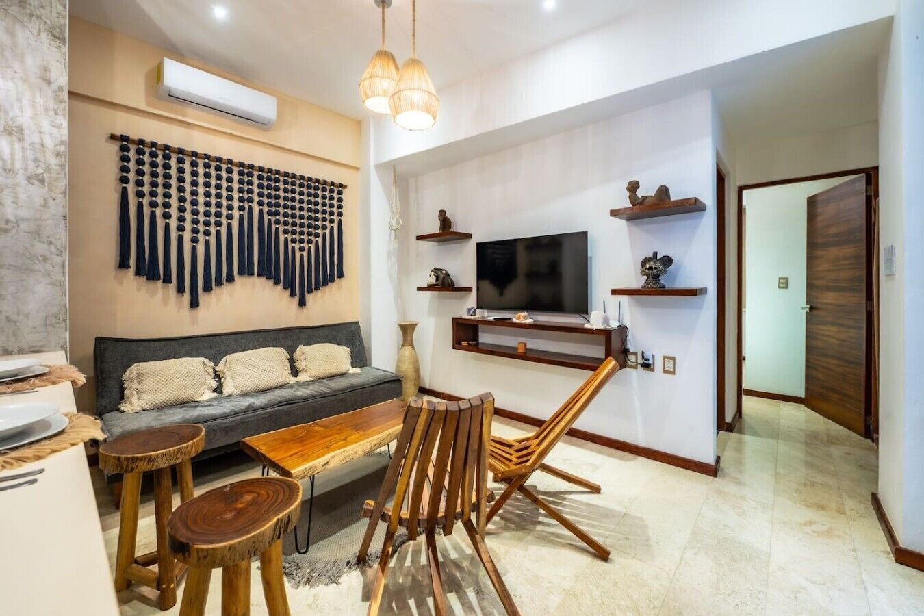 A modern living room with a sofa, wooden dining table, and chairs, a TV mounted on the wall, and decorative wall art.