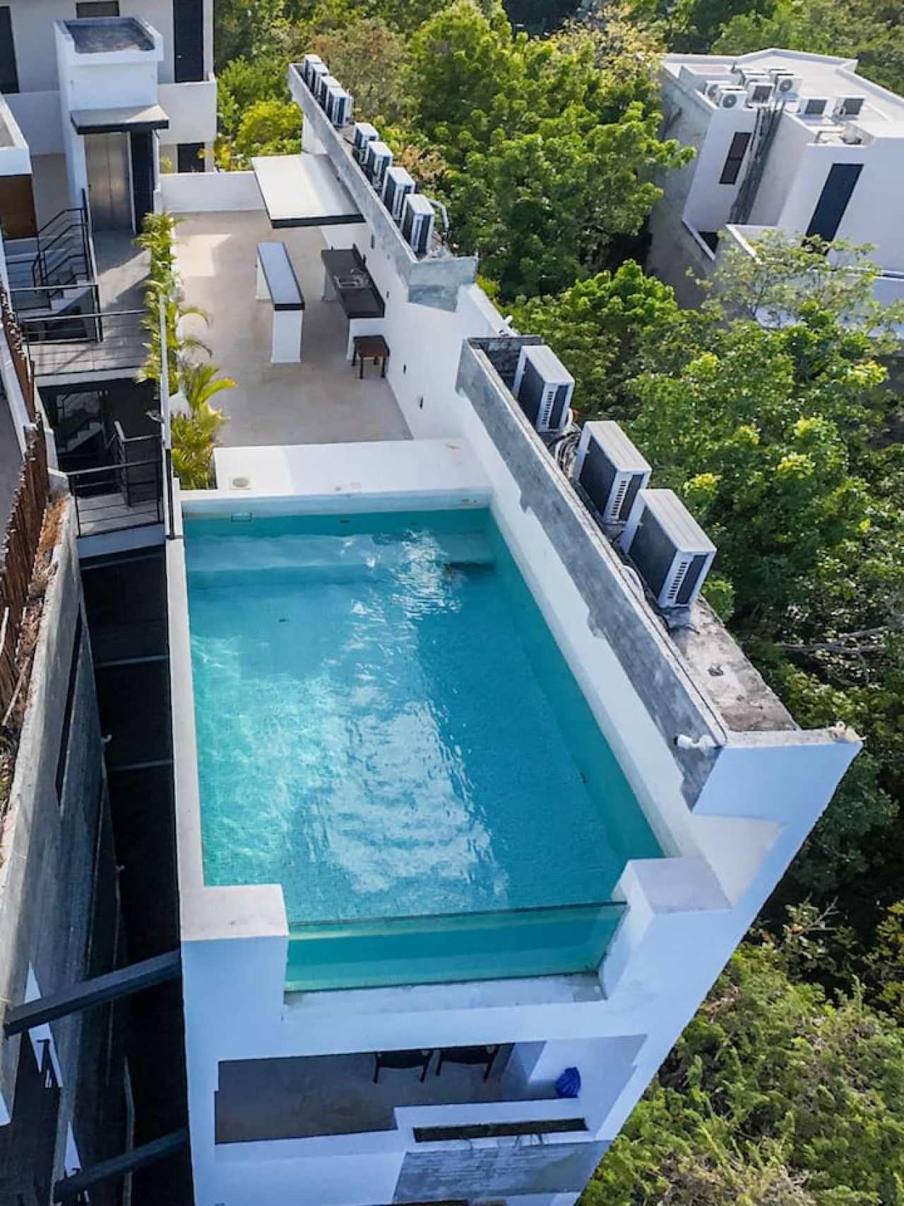 Ein Dachpool mit glasklarer blauer Wasserfläche, umgeben von einem weißen Gebäude mit Klimaanlagen.