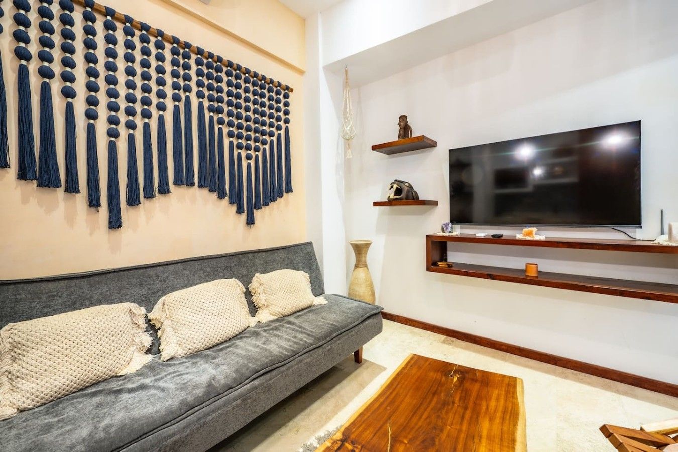 A modern living room with a grey sofa, a wall-mounted TV, and a decorative wall piece.