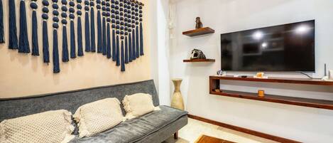 A modern living room with a grey sofa, a wall-mounted TV, and a decorative wall piece.