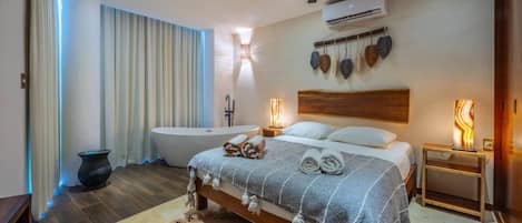 A modern bedroom with a large bed, a bathtub, and a ceiling fan.