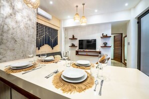 A modern kitchen with a marble backsplash, a dining area set for a meal, and a television on the wall. - Stylish 2BR Condo, Hot Tub, Gym & Rooftop Pool (Tulum)
