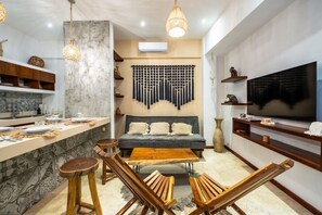 A modern kitchen with a dining area, a sofa, and a TV. - Stylish 2BR Condo, Hot Tub, Gym & Rooftop Pool (Tulum)