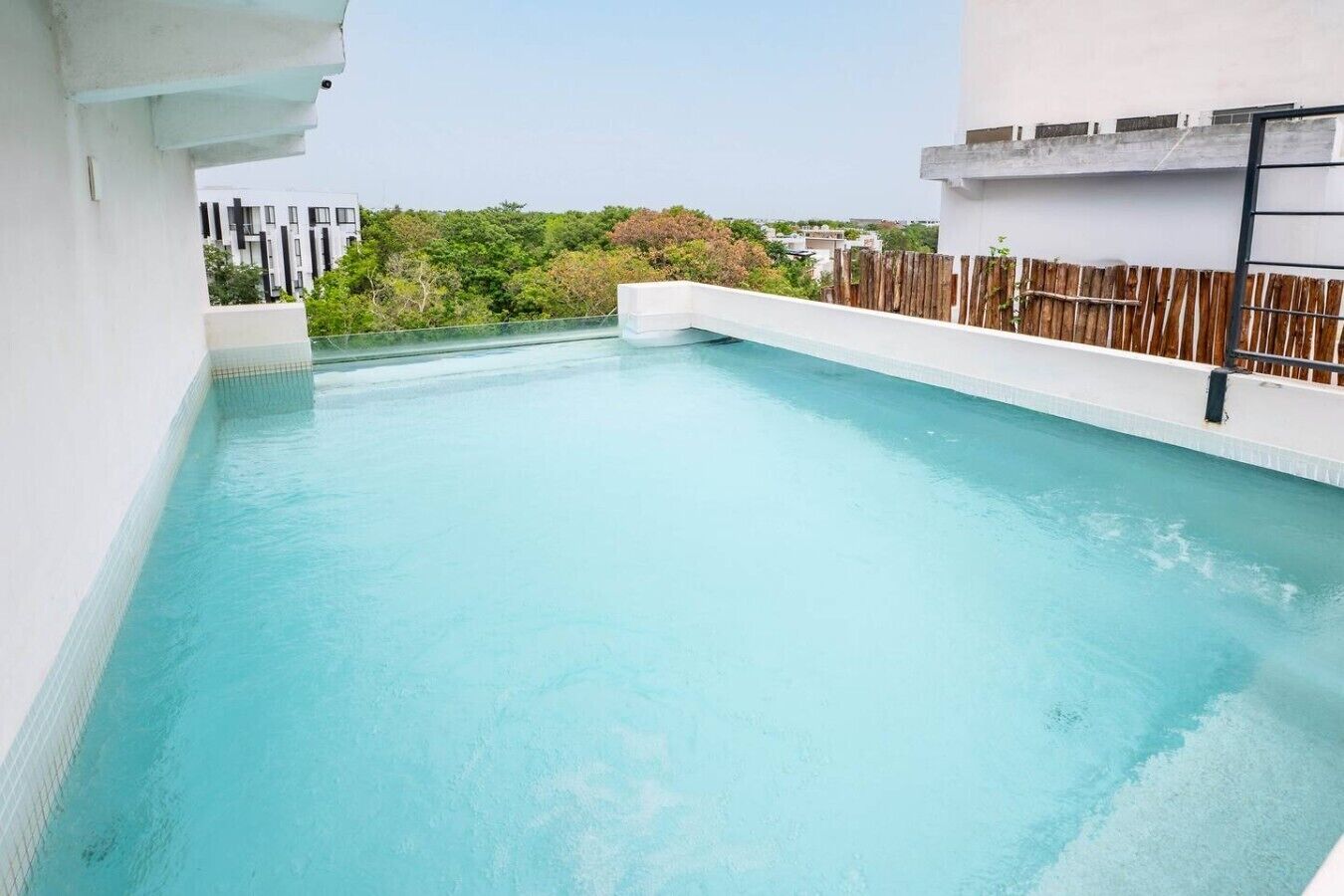 A rooftop swimming pool with a view of surrounding buildings and greenery.