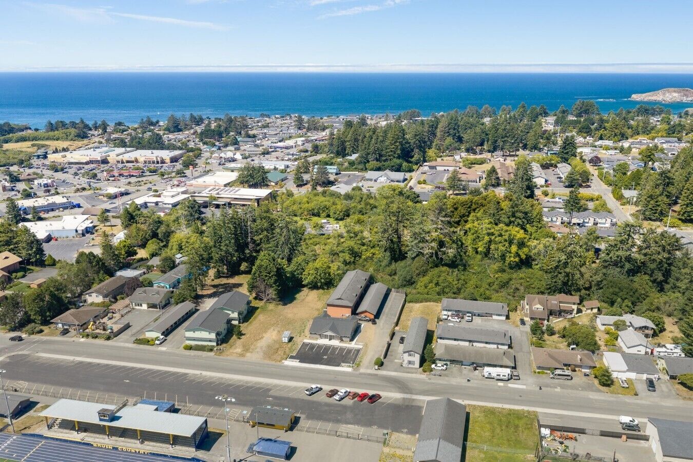 An aerial view of a coastal residential area with houses, roads, and a parking lot.