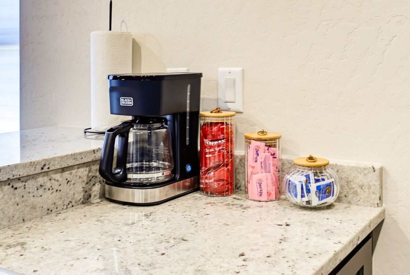 A kitchen counter with a coffee maker, a jar of red items, and two jars with lids.
