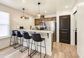 A modern kitchen with a central island, bar stools, and a dark door. - Seaside Nest-Cozy Coastal Retreat in Beautiful Brookings, Oregon (Brookings)