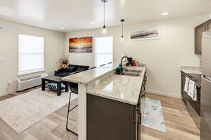 A modern kitchen with a granite countertop, stainless steel appliances, and a dining area with a black sofa and a coffee table. - Seaside Nest-Cozy Coastal Retreat in Beautiful Brookings, Oregon (Brookings)