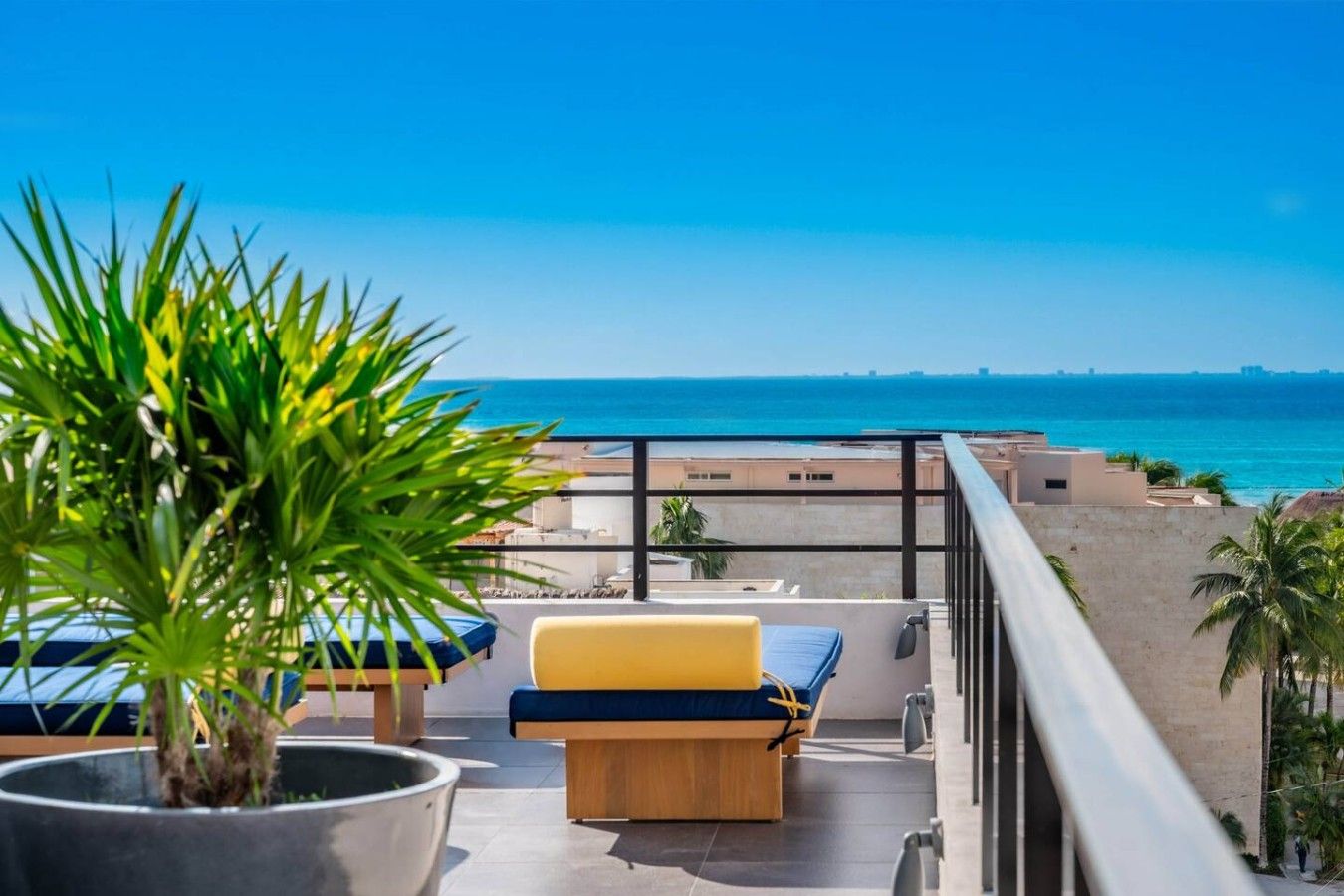 Ein Balkon mit Blick auf den Ozean, einer Topfpflanze und einem gelb-blauen Sofa.