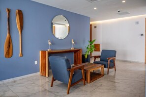 A modern lobby with a blue wall, wooden furniture, a round mirror, and a potted plant. - King Studio | Oceanview Pool & Gym | Free Parking (Playa del Carmen)