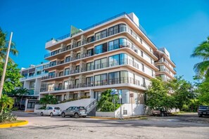 A multi-story hotel with balconies, a parking area, and a clear sky. - King Studio | Oceanview Pool & Gym | Free Parking (Playa del Carmen)
