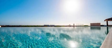 Une piscine d’eau cristalline, d’un bleu profond, d’où l’on aperçoit une côte lointaine et un bâtiment.