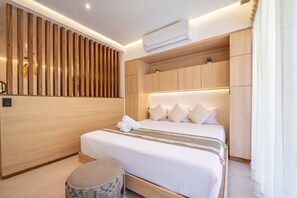 Ein modernes Hotelzimmer mit einem großen Bett, einer Wandpaneelausstattung aus Holz, einem eingebauten Kleiderschrank und einem runden Pouf.