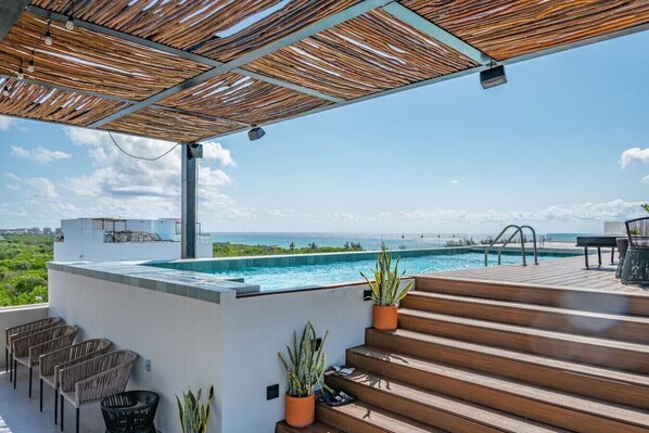 Ein Pool auf dem Dach mit Blick aufs Meer, eine Holzterrasse und Sitzmöglichkeiten im Freien.