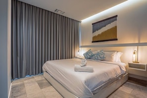 A hotel room with a large bed, a headboard with a painting, a nightstand with a lamp, and a curtain. - Luxury Beach Condo w/Rooftop Pool, Gym & Parking (Playa del Carmen)
