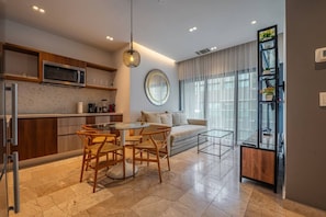 A modern kitchen with a dining area, a sofa, and a glass coffee table. - Luxury Beach Condo w/Rooftop Pool, Gym & Parking (Playa del Carmen)