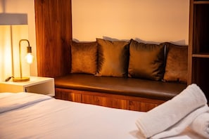 Une chambre d’hôtel avec un banc en bois, une lampe de chevet et un lit soigneusement fait.