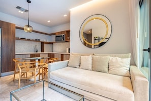 A modern living room with a sofa, a dining table with chairs, a kitchen area, and a large mirror on the wall. - Luxury Beach Condo w/Rooftop Pool, Gym & Parking (Playa del Carmen)