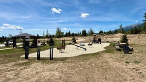 Un'area giochi all'aperto con altalene, scivoli e strutture per arrampicarsi, immersa tra alberi e con un cielo sereno.
