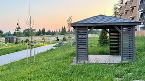 A gazebo with a slatted roof and a wooden deck, surrounded by grass and a paved path. - Lovely 1-bedroom apartment in Gerlachov perfect for a relaxing stay (Gerlachov)