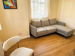A living room with a grey sectional sofa, a white armchair, and a wooden floor. - 3 Bedroom 2 Bathroom flat. 15mins walk to Wembley Stadium. Secure gated parking. (Wembley)