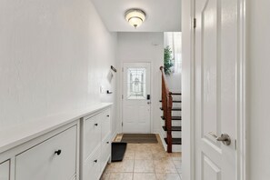 A hallway with a white door, a wooden staircase, and a light fixture on the ceiling. - Stylish 2-bedroom, 3-bath townhouse about 15 minutes from Niagara Falls. (St. Catharines)