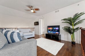 A living room with a grey sofa, a white rug, a TV on a stand, a ceiling fan, and a potted plant. - Stylish 2-bedroom, 3-bath townhouse about 15 minutes from Niagara Falls. (St. Catharines)