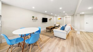 Ein modernes Wohnzimmer mit einem weißen Sofa, blauen Sesseln, einem Couchtisch und einem Flachbildfernseher an der Wand.