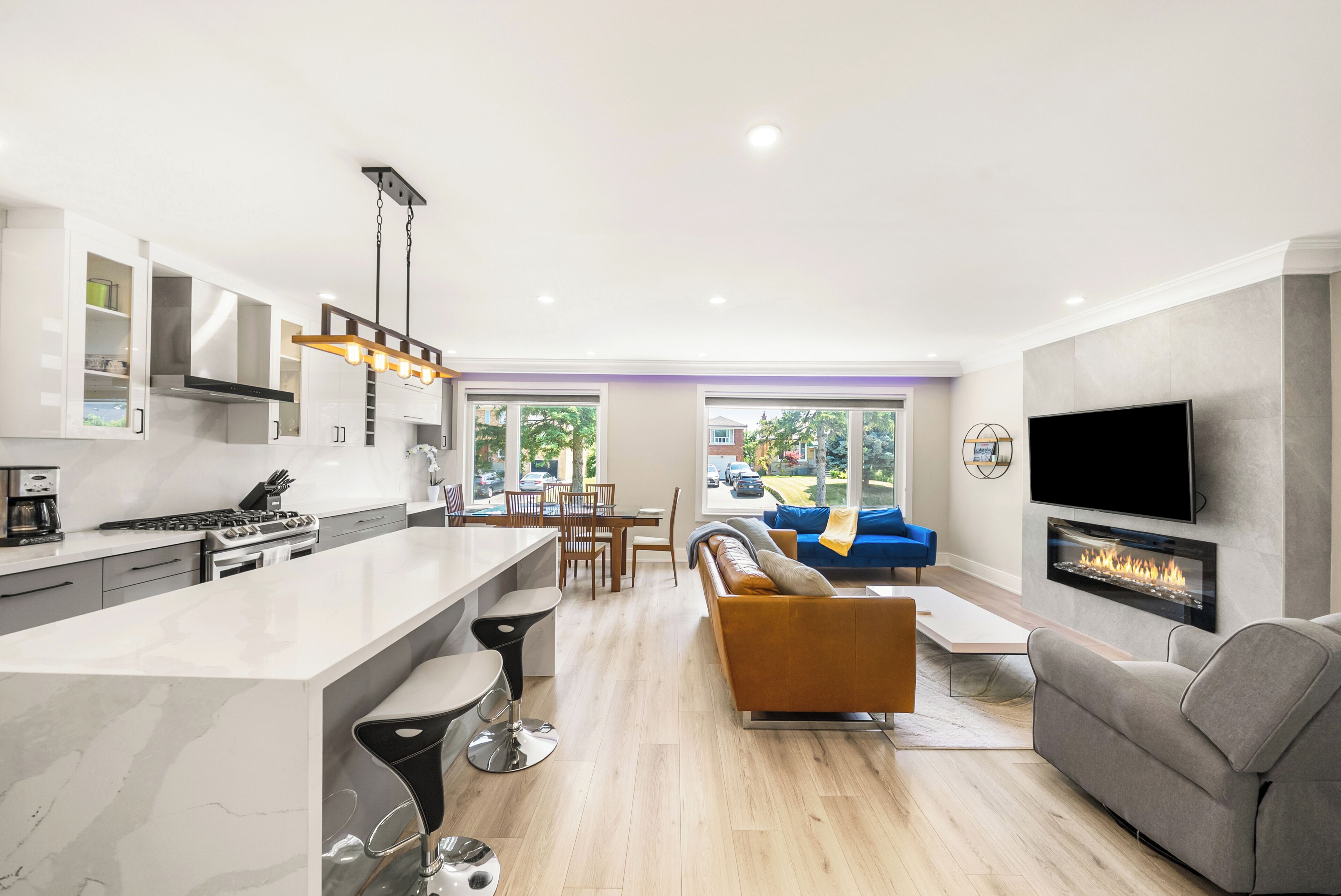 A modern kitchen with a central island, a dining area with a blue sofa, and a living room with a fireplace.