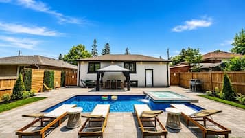 A backyard with a swimming pool, lounge chairs, and a covered patio area.