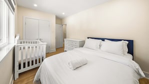 Ein Schlafzimmer mit einem Babybett, einer Kommode und einem Bett mit weißer Bettwäsche.