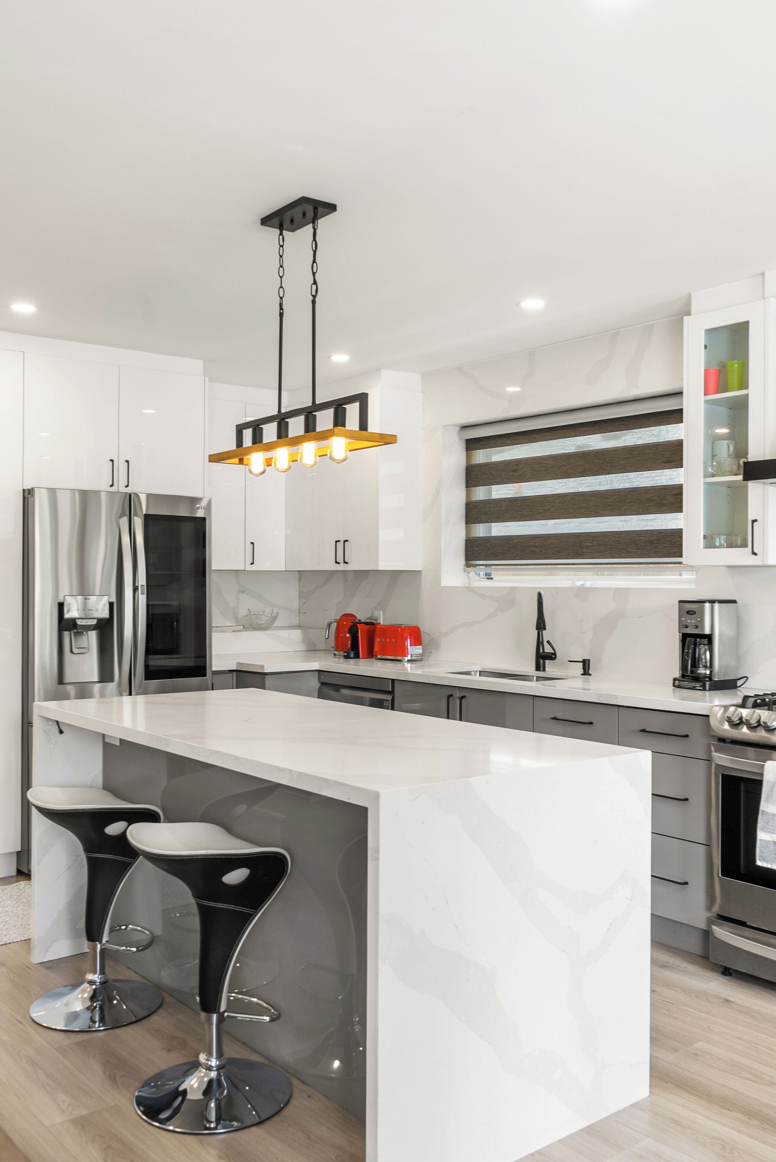 A modern kitchen with a central island, stainless steel appliances, and a hanging light fixture.