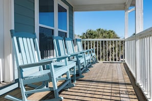A covered porch with blue Adirondack chairs and a wooden deck. - Pet Friendly with Gulf Views- 50 Sea Turtle by Royal Destinations (Santa Rosa Beach)